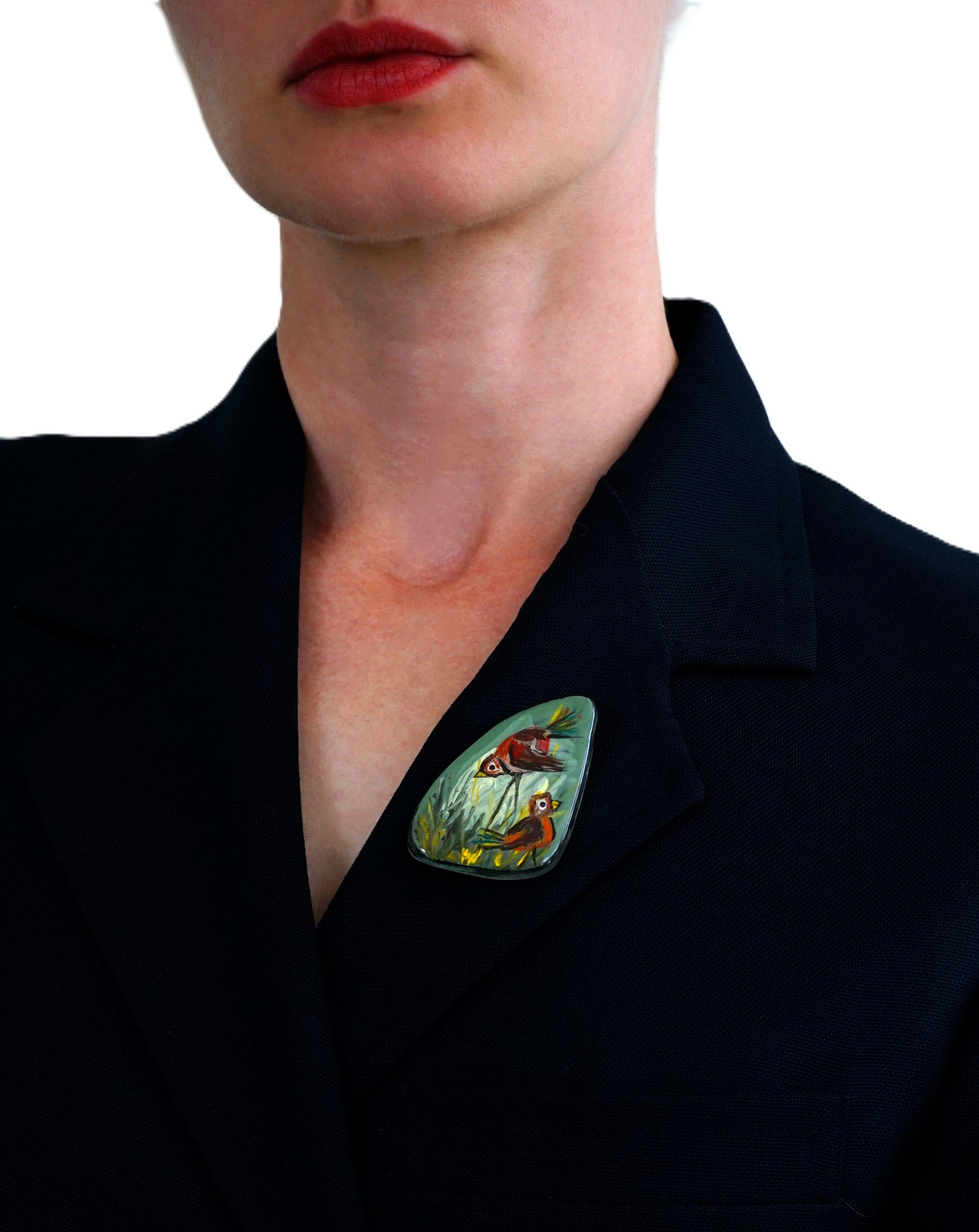 Person wearing a black blazer with a colorful brooch on a white background